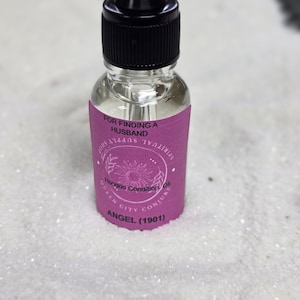 May include: A clear glass bottle with a black dropper top and a purple label. The label reads "FOR FINDING A HUSBAND" and "ANGEL (1901)". The bottle is filled with a clear liquid.