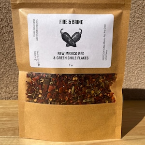 May include: A brown paper bag with a clear window showing red and green chili flakes. The bag has a label that says "Fire & Brine" and "New Mexico Red & Green Chile Flakes".