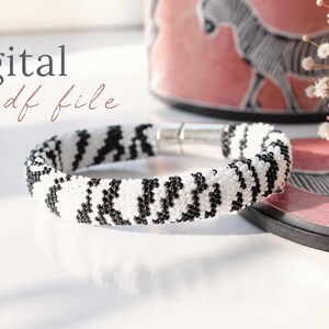 May include: A black and white beaded bracelet with a zebra stripe design and a silver magnetic clasp. The words "digital pdf file" are written in cursive. A pink decorative item with a zebra print is in the background.