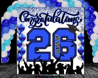May include: A graduation backdrop with the words "Congratulations" and "Class of 26" in blue and black. The backdrop is decorated with blue, white, and teal balloons, and a silhouette of graduates. The backdrop is supported by a metal stand.