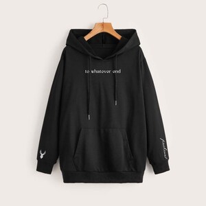 K&ouml;nnte beinhalten: Schwarzer Kapuzenpullover mit einer K&auml;ngurutasche und wei&szlig;em Text, der "to whatever end" lautet. Der linke &Auml;rmel hat ein kleines wei&szlig;es Hirschmotiv und der rechte &Auml;rmel hat das Wort "freeflow" in Wei&szlig;.