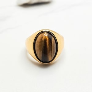 May include: A gold ring with a brown and gold oval tiger's eye gemstone.