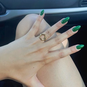 May include: A hand wearing a gold ring with an open circle design. The fingernails are painted a bright green.