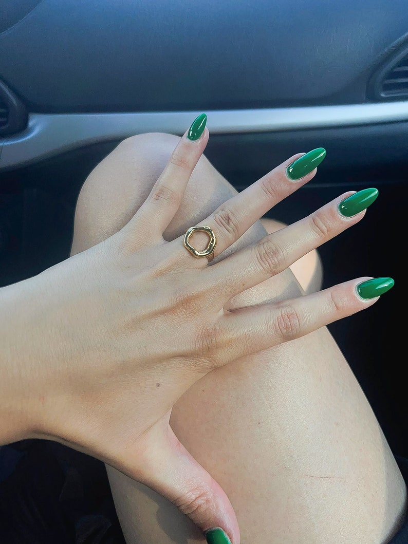 May include: A hand wearing a gold ring with an open circle design. The fingernails are painted a bright green.