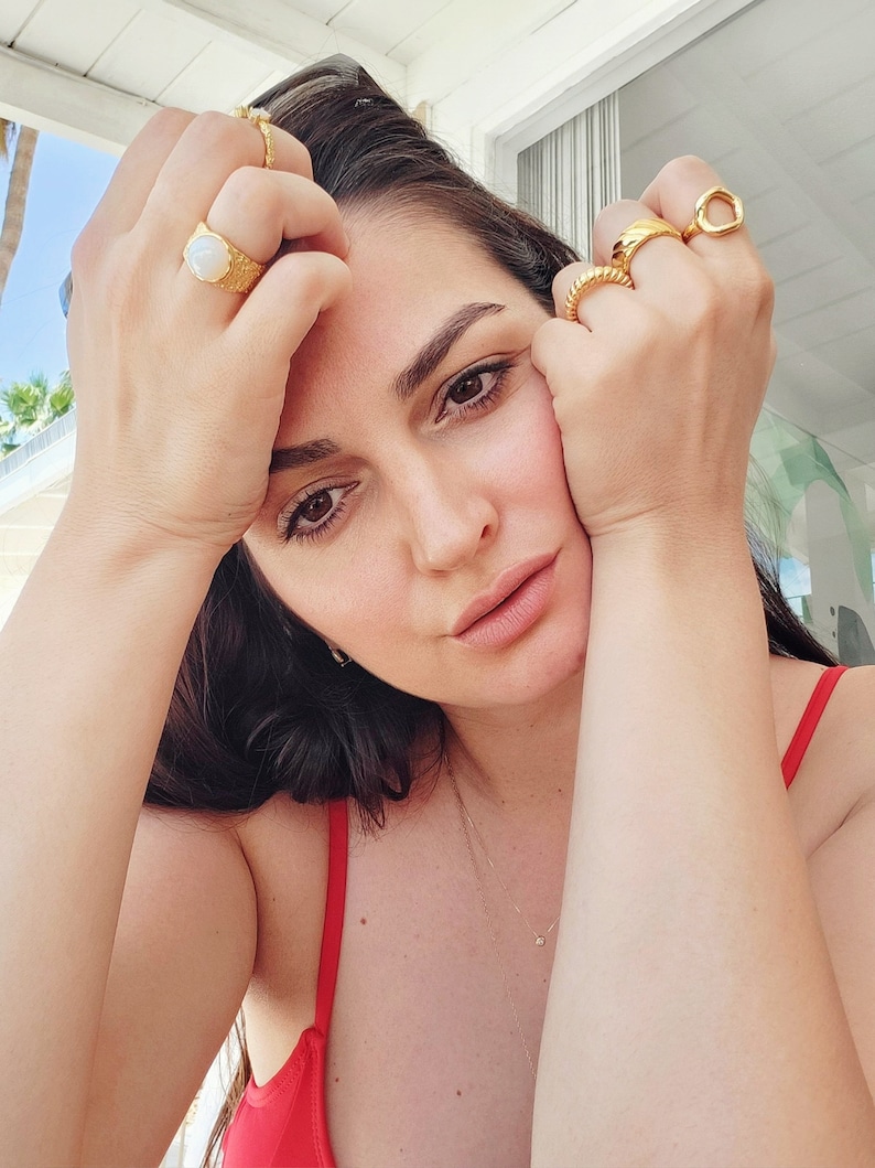 Female model wears chunky gold rings on her hands