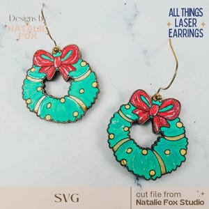 May include: A pair of laser-cut earrings featuring a Christmas wreath design. The wreaths are painted in shades of green with red bows and gold accents. The earrings are suspended from gold-colored ear wires. Text on the image reads "ALL THINGS LASER EARRINGS".