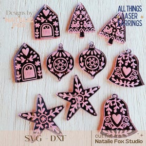Puede incluir: Adornos navideños cortados con láser en formas de casas, árboles, campanas y estrellas. Los adornos son negros con detalles rosas y diseños decorativos. Se puede leer el texto "ALL THINGS LASER RINGS".