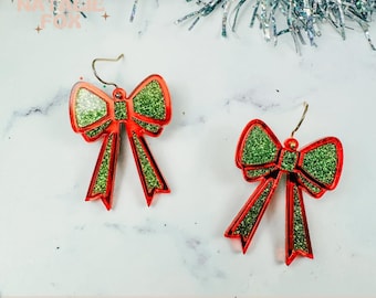 May include: A pair of red and green glitter bow earrings. The bows are tied with a red ribbon and have a gold hook.