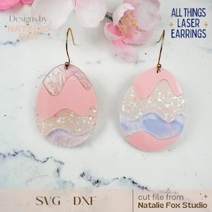 May include: A pair of pink and white layered egg-shaped earrings with gold hooks. The earrings have a glittery finish and are designed to look like Easter eggs. The text "ALL THINGS LASER EARRINGS" is visible in the top right corner of the image.