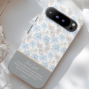 May include: A white phone case with a floral pattern in shades of blue and yellow. The case has a quote from Jesus on the bottom: "I am the light of the world. Whoever follows me will never walk in darkness, but will have the light of life." John 8:12