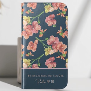 May include: A navy blue phone case featuring a floral pattern of pink and yellow orchids on stems. The case has a dark blue band at the bottom with the text "Be still and know that I am God. Psalm 46:10."