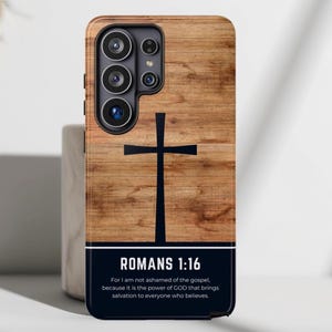 May include: A rectangular smartphone case featuring a light brown wood grain pattern with a black cross centered in the upper portion. The lower section is a solid black rectangle containing the white text ROMANS 1:16 and the full verse.