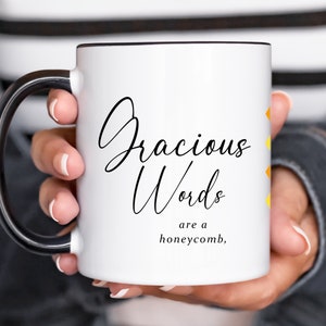 May include: White ceramic mug with a black handle. The mug has black text that reads "Gracious Words are a honeycomb" with a yellow and orange design on the side.