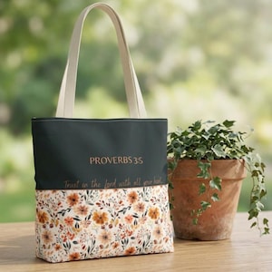 May include: A dark green tote bag with two beige handles, featuring the text "PROVERBS 3:5 Trust in the Lord with all your heart" in a copper-colored font. The bottom section of the bag displays a floral pattern with orange and brown flowers.