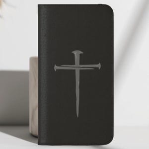 May include: Black leather phone case featuring a gray cross design. The cross is a simple, stylized illustration. The case has a textured surface and a rectangular shape. The case is designed to protect a phone.