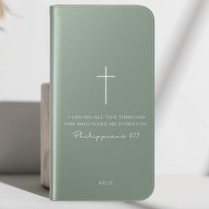 May include: Pale green Bible cover featuring a white cross and the inscription "I CAN DO ALL THIS THROUGH HIM WHO GIVES ME STRENGTH. Philippians 4:13" and the name "KYLIE".