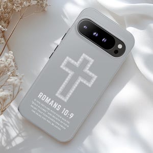 Może przedstawiać: Jasnoszara obudowa telefonu z błyszczącym wzorem krzyża. Obudowa ma napis "ROMANS 10:9" i werset biblijny wydrukowany na biało. Obudowa telefonu znajduje się na białej powierzchni.
