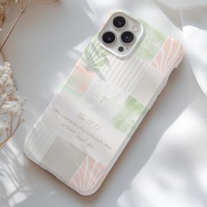 May include: A phone case with a patchwork design in pastel colors, including green, pink, and white. The case features the text "John 15:12" and a quote about love. The case has a camera cutout and is designed for a smartphone.