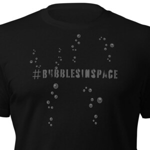 Può includere: Maglietta nera con una grafica bianca di bolle e il testo "#BUBBLESINSPACE".
