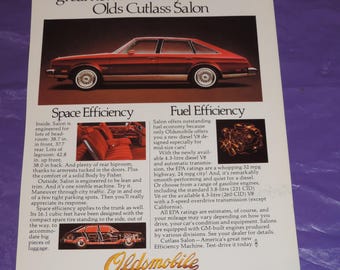 May include: A vintage print advertisement for the Oldsmobile Cutlass Salon. The ad features a red car with a white interior and the text "Introducing America's great new Efficiency Machine: Olds Cutlass Salon". The ad highlights the car's fuel efficiency and spacious interior.