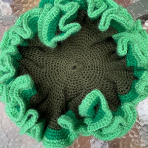 May include: A crocheted coral reef decoration in shades of green. The coral is made with a textured, bumpy yarn and has a ruffled edge.