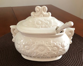 May include: White ceramic soup tureen with a floral design and a lid. The tureen has a matching ladle.