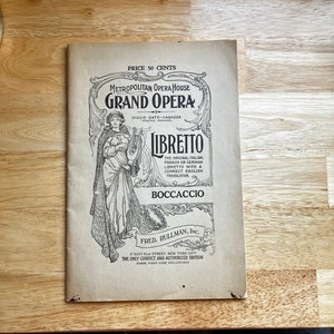 May include: A black and white image of a vintage program for the Metropolitan Opera House Grand Opera. The program features a woman holding a lyre and the title "Libretto Boccaccio".