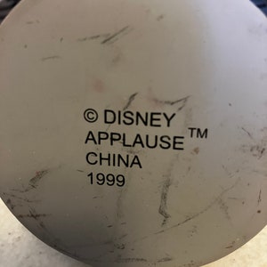 May include: A white ceramic figurine base with the text "&copy; DISNEY APPLAUSE&trade; CHINA 1999" printed on it.