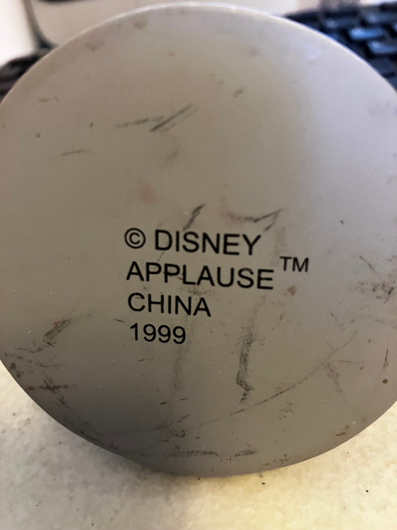 May include: A white ceramic figurine base with the text "&copy; DISNEY APPLAUSE&trade; CHINA 1999" printed on it.