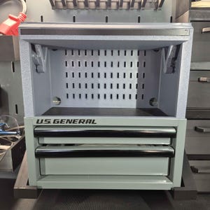May include: A gray U.S. General tool storage unit featuring an open top shelf with a perforated back panel and two lower drawers with black horizontal handles. The unit has a metallic finish and a rectangular frame design for organizing tools.