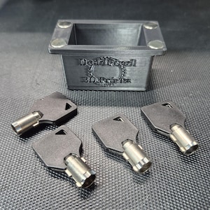 May include: A rectangular dark gray 3D-printed container with four silver circular magnets embedded in the top corners. The front features the embossed text "DeadPixel 3D Prints". Three black and silver tubular keys are arranged in front.
