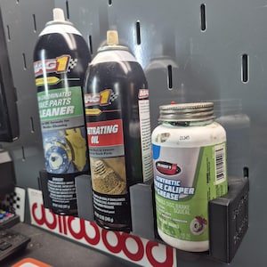 Op de afbeelding: Een zwarte 3D-geprinte wandorganizer met drie auto-onderhoudsproducten: een 397g Mag 1 remmenreiniger, een 340g Mag 1 kruipolie spuitbus en een 227g Johnsen's synthetisch remklauwvetsmeermiddel in een pot.