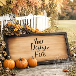 May include: A wooden sign with a black frame sits on a wooden surface in front of a white picket fence. The sign has the text "Your Design Here" written on it. Three orange pumpkins are in front of the sign.