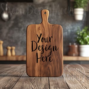 Könnte beinhalten: Ein Schneidebrett aus Holz mit einem Griff, das auf einem Holztisch steht. Das Brett hat den Text "Your Design Here" eingraviert.