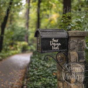 May include: Black mailbox with a white inscription that reads "Your Design Here" mounted on a stone wall. The mailbox is in a wooded area with a path leading away from it.