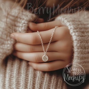 May include: A silver necklace with a round pendant that says "Your Design Here" on it. The necklace is being held by a person wearing a beige sweater.