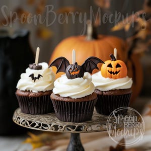 Peut inclure: Trois cupcakes au chocolat décorés de glaçage blanc et de décorations sur le thème d'Halloween. Les décorations comprennent une chauve-souris avec un visage de citrouille, une citrouille et une chauve-souris. Les cupcakes sont sur un support à gâteau argenté.