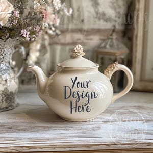 Könnte beinhalten: Eine weiße Teekanne aus Keramik mit goldenen Akzenten und einer goldenen Krone auf dem Deckel. Die Teekanne hat einen Text "Your Design Here" an der Seite.