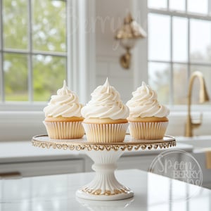 Könnte beinhalten: Drei weiße Cupcakes mit Vanille-Frosting werden auf einem weißen Kuchenständer mit goldenem Rand präsentiert. Der Ständer hat eine weiße Sockelbasis. Die Cupcakes befinden sich auf einer weißen Oberfläche.