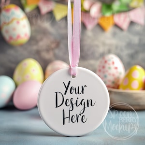 May include: A white, round ceramic ornament with the text "Your Design Here" in black script, hanging from a pink ribbon. The background features colorful Easter eggs and a banner, creating a festive holiday theme.