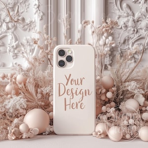 May include: White phone case with a camera lens and the text "Your Design Here" in a light brown font. The case is surrounded by dried flowers and beige decorative balls.