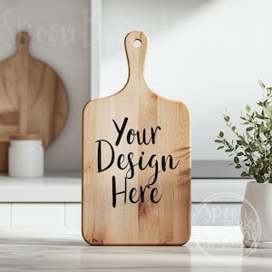 May include: A wooden cutting board with a handle, ready for customization. The board is light brown and has the text "Your Design Here" printed in black.