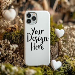 May include: White phone case with a camera lens and the text "Your Design Here" on a background of dried flowers and moss.