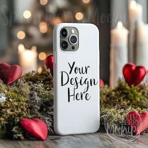 May include: White phone case with a black camera lens and the text "Your Design Here" on a white background. The phone case is surrounded by red hearts and green moss.
