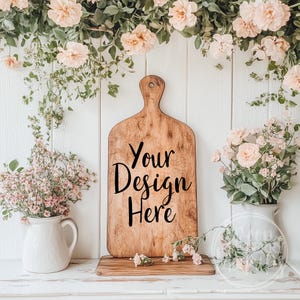 May include: A wooden chopping board with the text "Your Design Here" in black lettering. The board is surrounded by pink flowers and greenery.