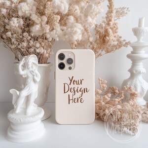 May include: A white iPhone case with a brown text overlay that says "Your Design Here". The case is sitting on a white surface with dried flowers and a white statue.