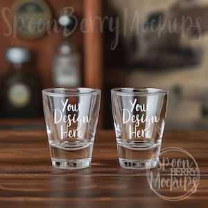 Könnte beinhalten: Zwei klare Glas-Schnapsgläser mit dem Text "Your Design Here" auf der Vorderseite. Die Gläser stehen auf einer Holzoberfläche.