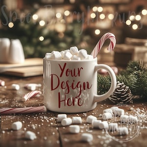 Może przedstawiać: Biały ceramiczny kubek z czerwonym napisem "Your Design Here", wypełniony gorącą czekoladą i piankami, z wystającą z kubka laską cukrową, oraz rozrzuconymi piankami na drewnianym stole.