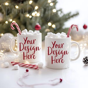 Może przedstawiać: Dwa białe kubki wypełnione piankami i ozdobione cukrowymi laskami. Kubki stoją na białym tle z choinką w tle. Na każdym kubku widnieje napis "Your Design Here".