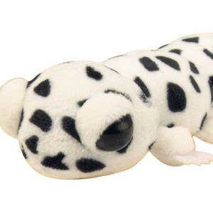 May include: A plush toy shaped like a Dalmatian dog. The toy is white with black spots and has large, black eyes. It has small, rounded ears and a small tail. The toy is made of a soft, fuzzy material.